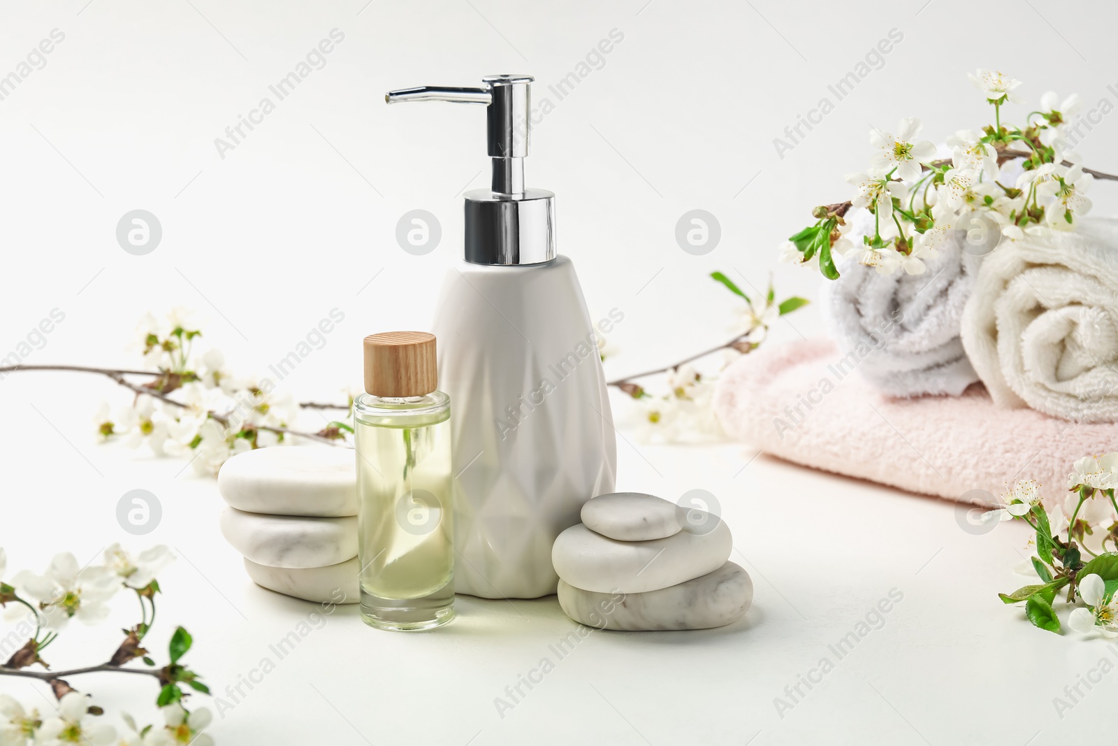 Spa products, pebble stones and twigs with beautiful flowers on white table, closeup Photo of Spa products, pebble stones and twigs with beautiful flowers on white table, closeup