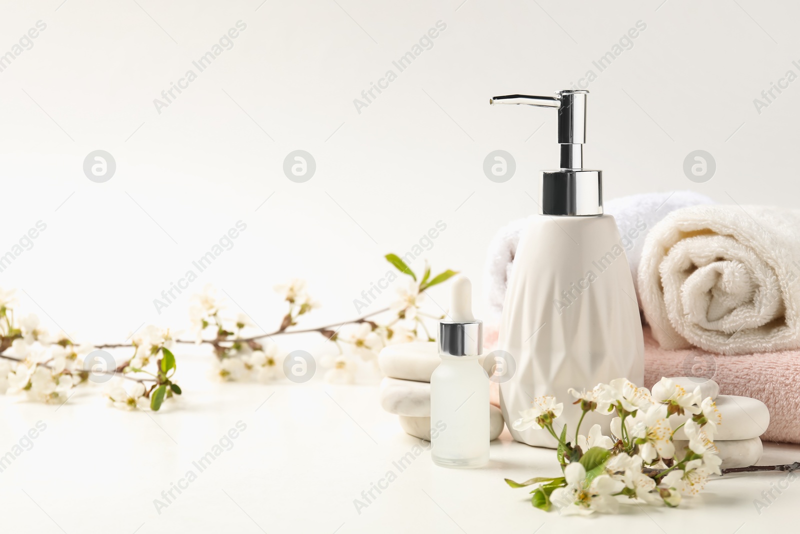 Spa products, pebble stones and twigs with beautiful flowers on white table, closeup Photo of Spa products, pebble stones and twigs with beautiful flowers on white table, closeup