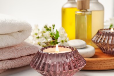 Photo of Burning candles and spa products on white table, selective focus