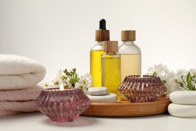 Photo of Spa products, burning candles, pebble stones and twigs with beautiful flowers on white table, closeup