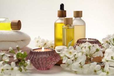 Photo of Spa products, burning candles and twigs with beautiful flowers on white table, closeup