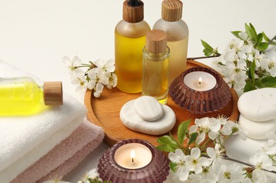 Photo of Spa products, burning candles, pebble stones and twigs with beautiful flowers on white table, closeup
