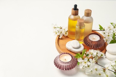 Photo of Spa products, burning candles, pebble stones and twigs with beautiful flowers on white background. Space for text