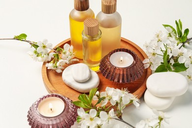 Photo of Spa products, burning candles, pebble stones and twigs with beautiful flowers on white table, closeup