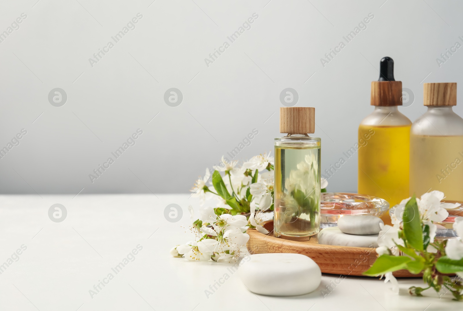Spa products, pebble stones and twigs with beautiful flowers on white table against grey background, closeup. Space for text Photo of Spa products, pebble stones and twigs with beautiful flowers on white table against grey background, closeup. Space for text