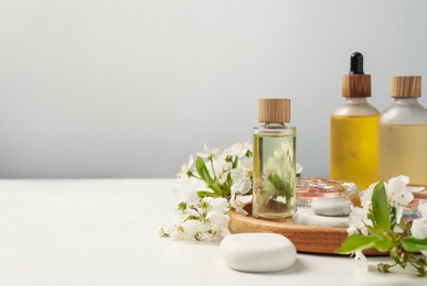 Photo of Spa products, pebble stones and twigs with beautiful flowers on white table against grey background, closeup. Space for text