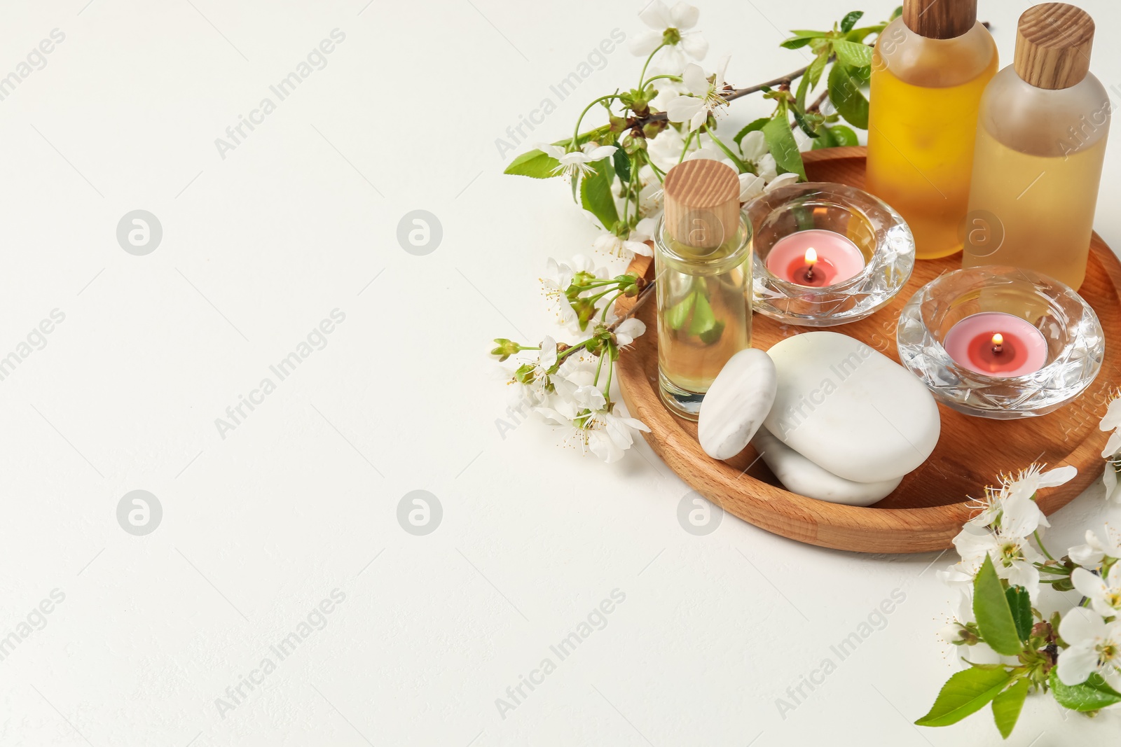 Spa products, burning candles, pebble stones and twigs with beautiful flowers on white background. Space for text Photo of Spa products, burning candles, pebble stones and twigs with beautiful flowers on white background. Space for text