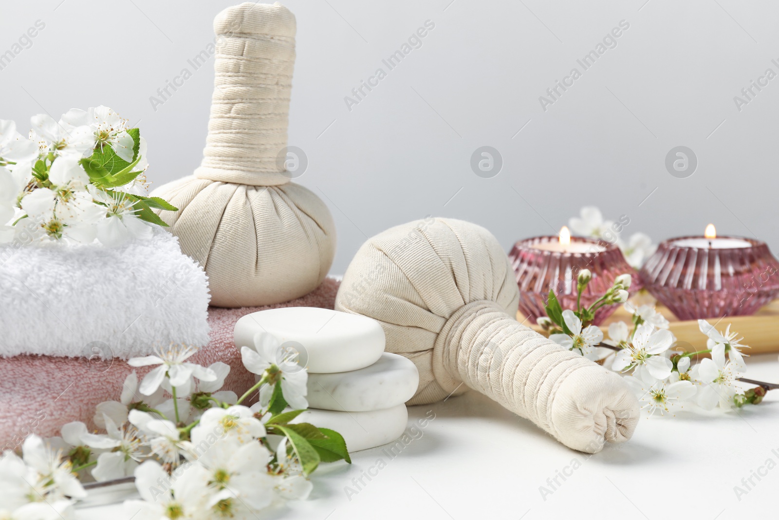 Spa products, pebble stones and twigs with beautiful flowers on white table against grey background, closeup Photo of Spa products, pebble stones and twigs with beautiful flowers on white table against grey background, closeup