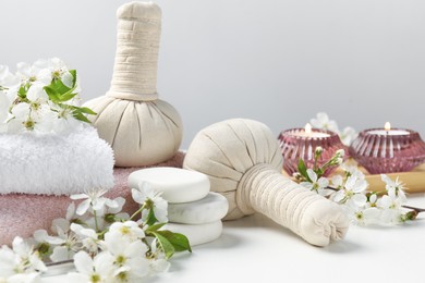Photo of Spa products, pebble stones and twigs with beautiful flowers on white table against grey background, closeup