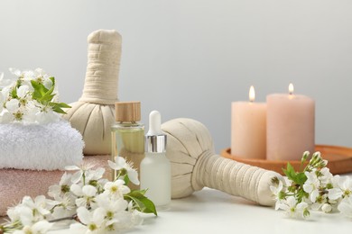 Photo of Spa products and twigs with beautiful flowers on white table against grey background, closeup