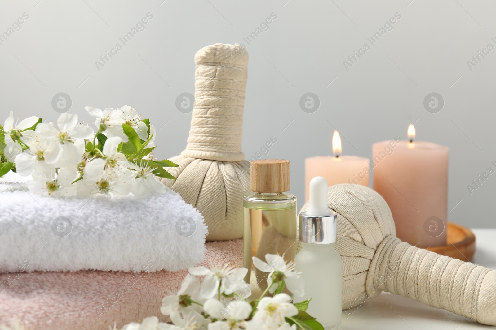 Spa products and twigs with beautiful flowers on white table against grey background, closeup Photo of Spa products and twigs with beautiful flowers on white table against grey background, closeup