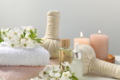 Photo of Spa products and twigs with beautiful flowers on white table against grey background, closeup