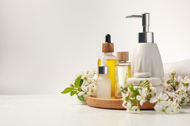 Photo of Spa products, pebble stones and twigs with beautiful flowers on white table, closeup. Space for text