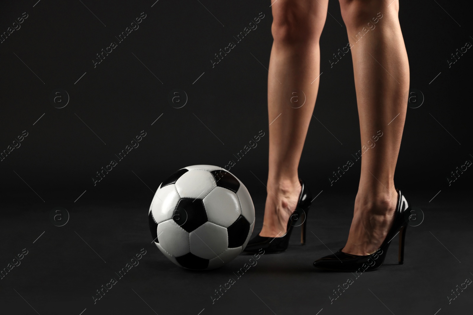 Photo of Woman in high heeled shoes with soccer ball on dark background, closeup