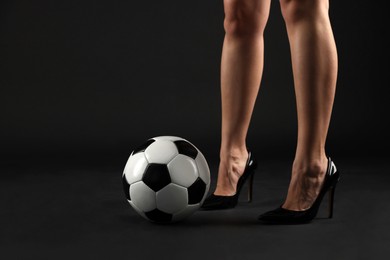 Photo of Woman in high heeled shoes with soccer ball on dark background, closeup