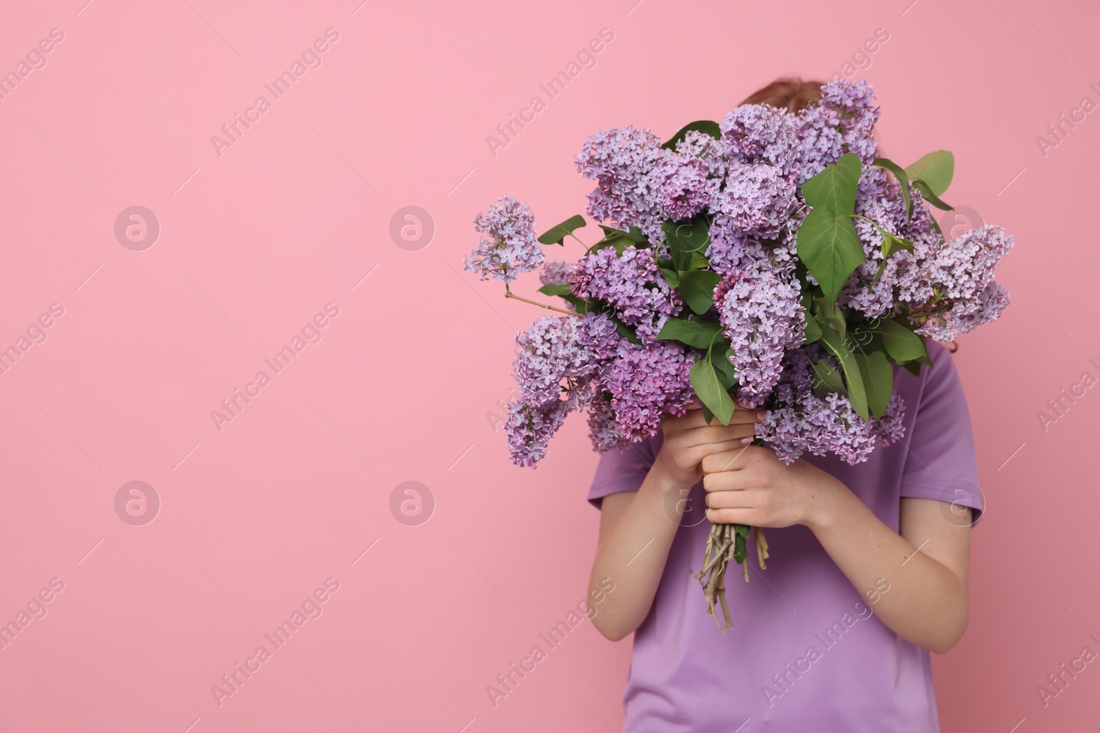 Teenage girl hiding behind bouquet of lilac flowers on pink background. Space for text Photo of Teenage girl hiding behind bouquet of lilac flowers on pink background. Space for text