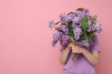 Photo of Teenage girl hiding behind bouquet of lilac flowers on pink background. Space for text