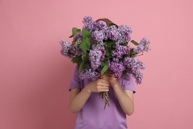 Photo of Teenage girl hiding behind bouquet of lilac flowers on pink background