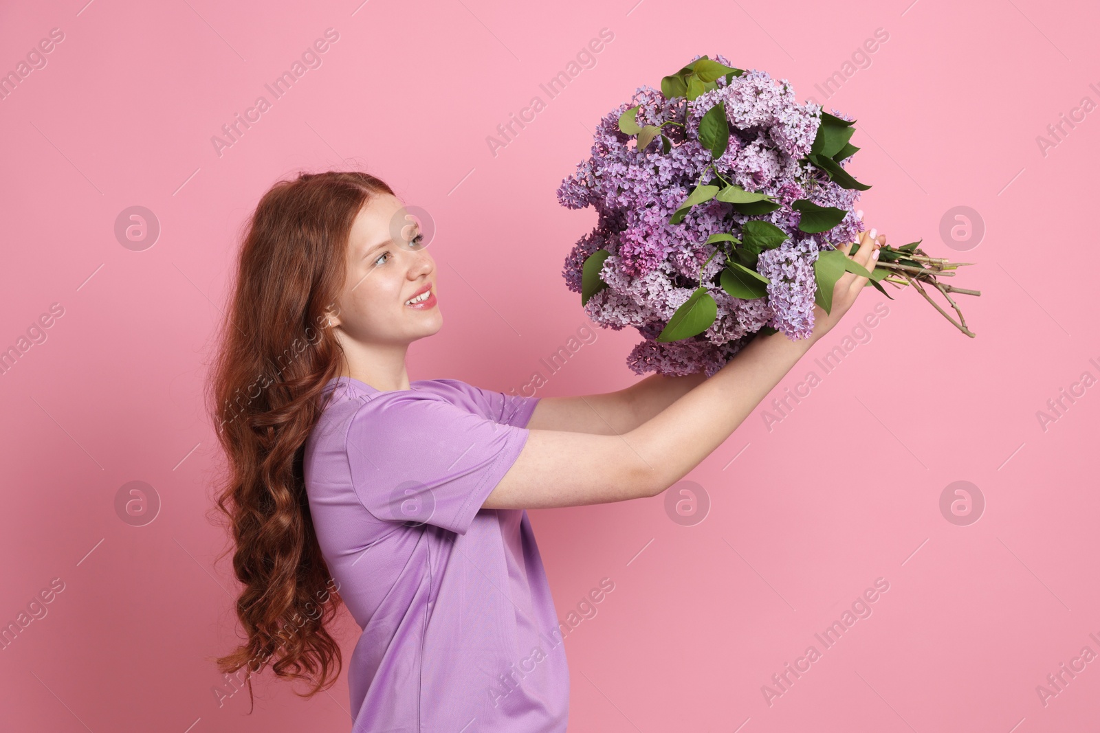 Smiling teenage girl with bouquet of lilac flowers on pink background Photo of Smiling teenage girl with bouquet of lilac flowers on pink background