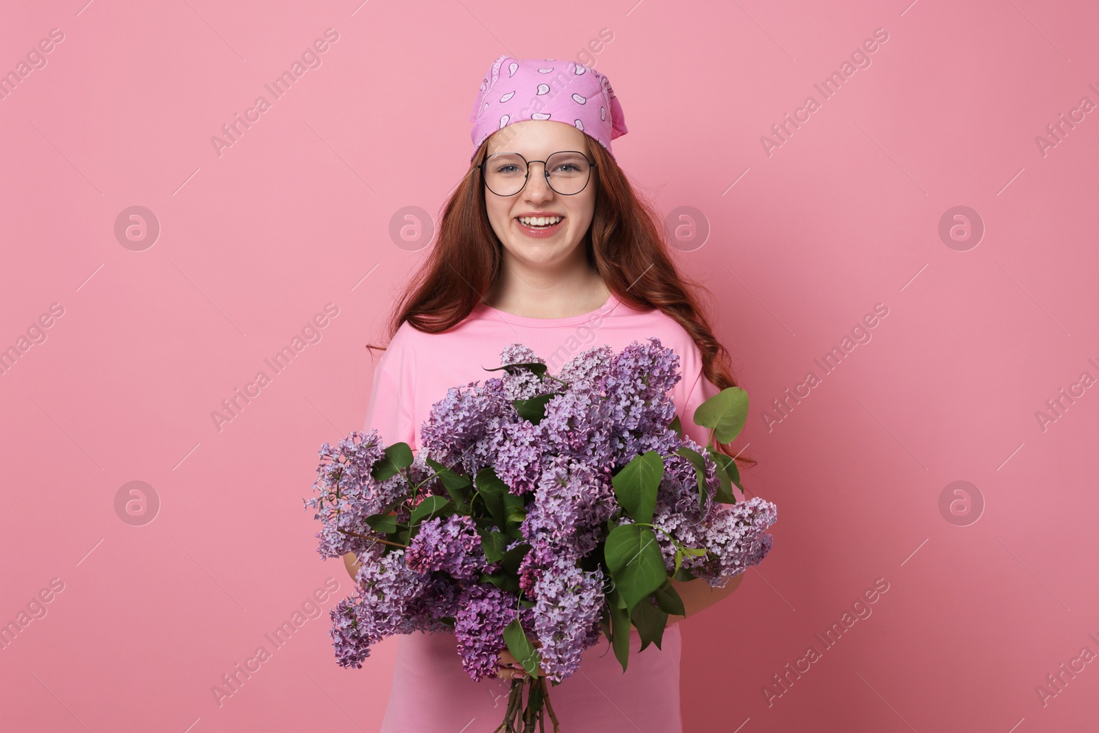 Portrait of smiling teenage girl with lilac flowers on pink background Photo of Portrait of smiling teenage girl with lilac flowers on pink background