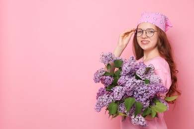 Photo of Smiling teenage girl with bouquet of lilac flowers on pink background. Space for text