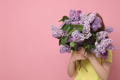 Photo of Teenage girl hiding behind bouquet of lilac flowers on pink background. Space for text