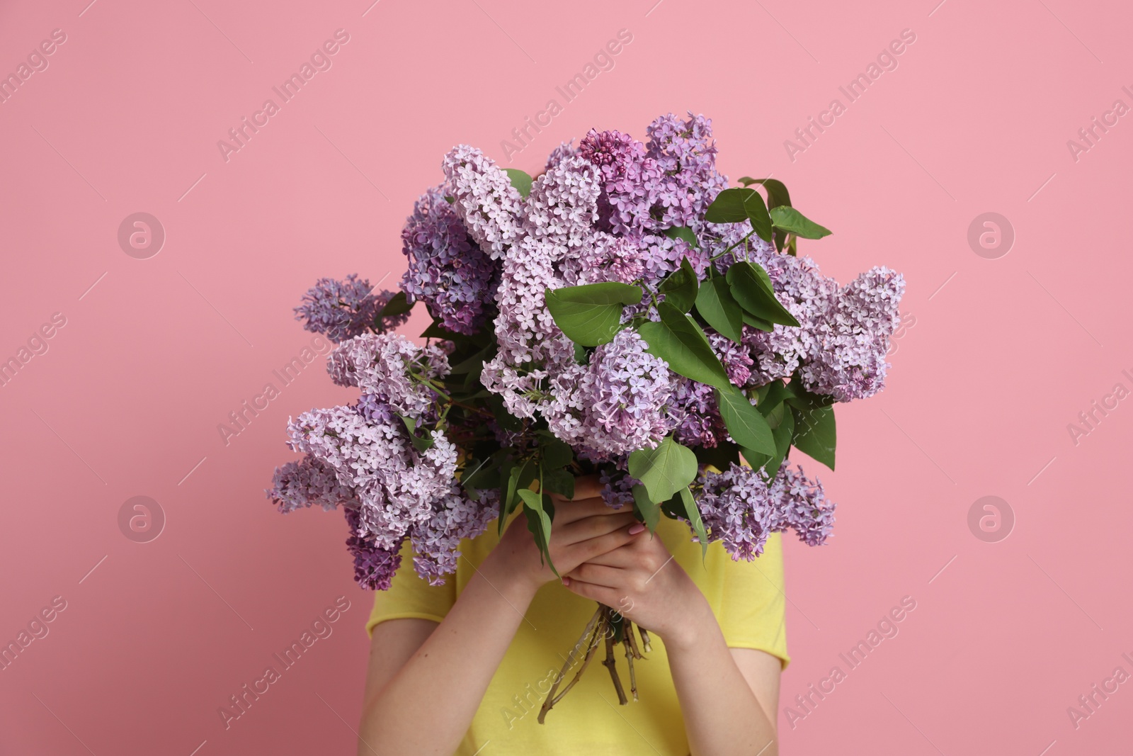 Teenage girl hiding behind bouquet of lilac flowers on pink background Photo of Teenage girl hiding behind bouquet of lilac flowers on pink background