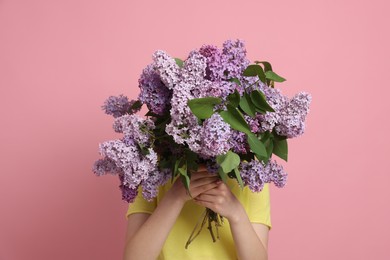 Photo of Teenage girl hiding behind bouquet of lilac flowers on pink background