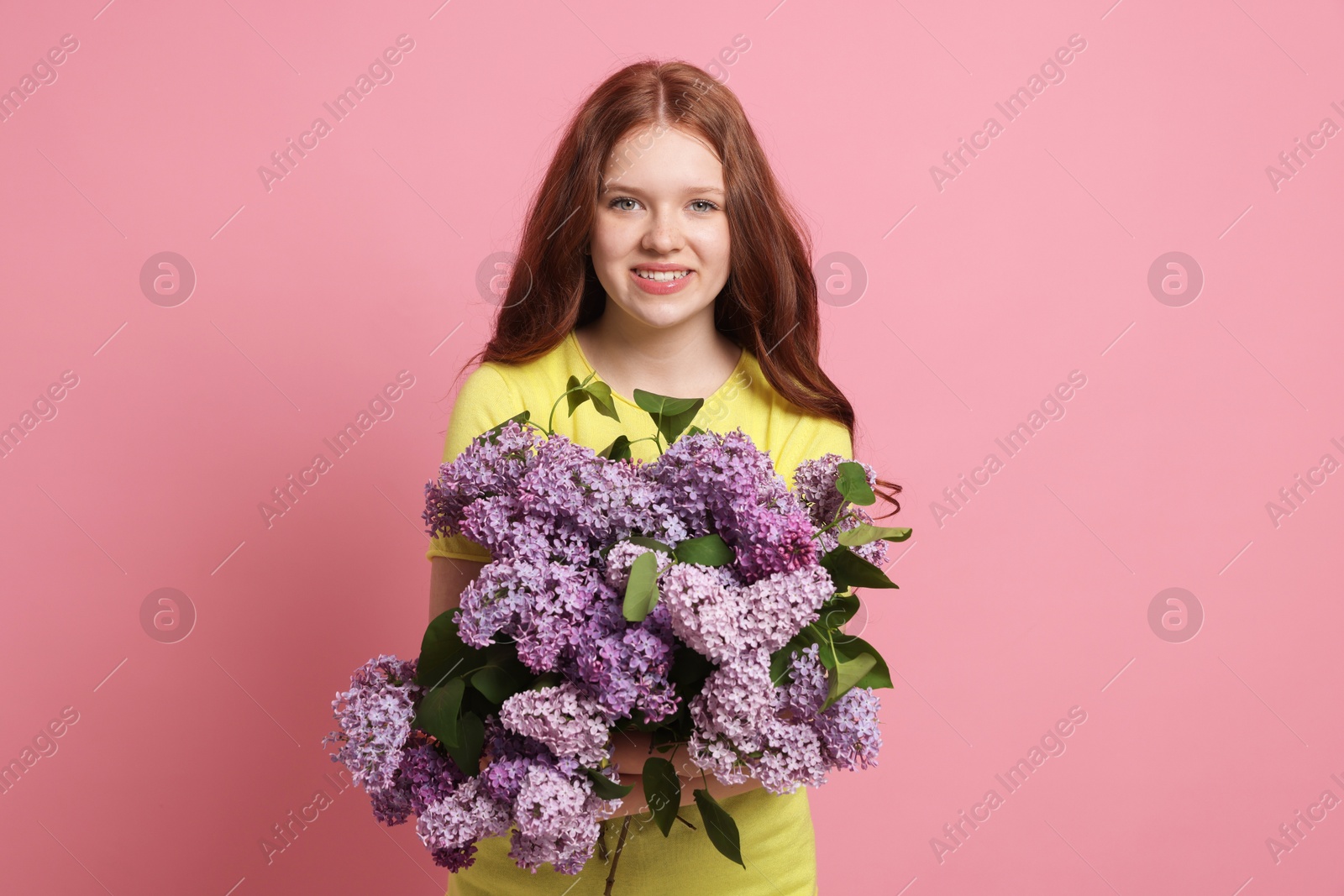 Portrait of smiling teenage girl with lilac flowers on pink background Photo of Portrait of smiling teenage girl with lilac flowers on pink background