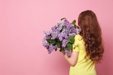 Photo of Teenage girl with bouquet of lilac flowers on pink background, back view. Space for text