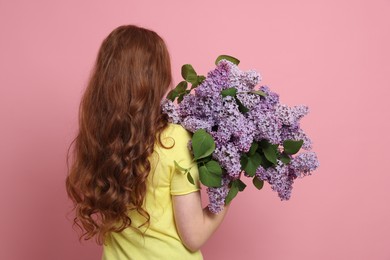 Photo of Teenage girl with bouquet of lilac flowers on pink background, back view