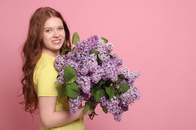 Photo of Smiling teenage girl with bouquet of lilac flowers on pink background. Space for text
