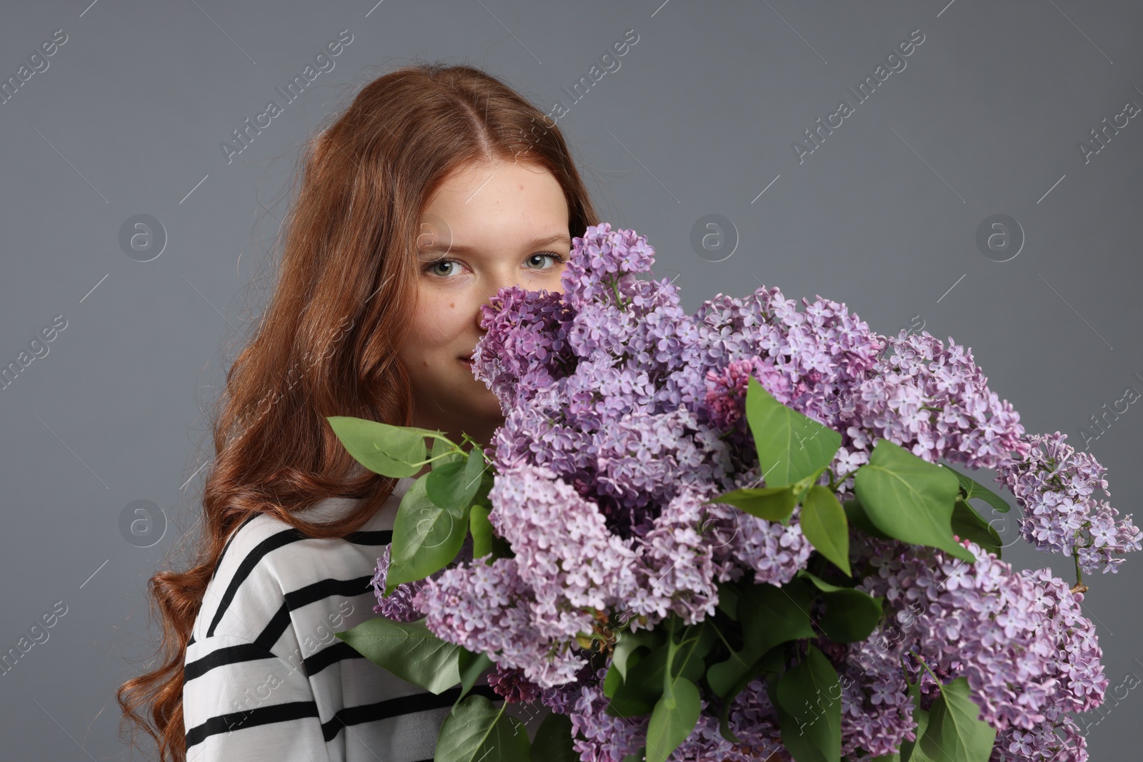 Portrait of beautiful teenage girl with lilac flowers on grey background Photo of Portrait of beautiful teenage girl with lilac flowers on grey background