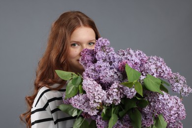 Photo of Portrait of beautiful teenage girl with lilac flowers on grey background