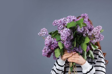 Photo of Teenage girl hiding behind bouquet of lilac flowers on grey background. Space for text