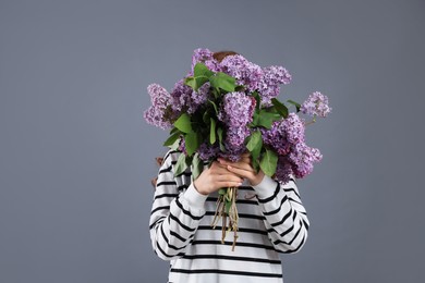 Photo of Teenage girl hiding behind bouquet of lilac flowers on grey background