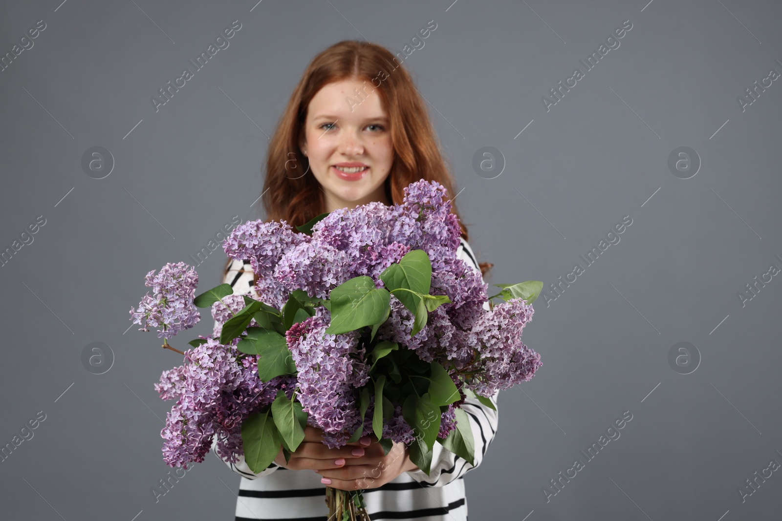 Smiling teenage girl with bouquet of lilac flowers on grey background, selective focus Photo of Smiling teenage girl with bouquet of lilac flowers on grey background, selective focus