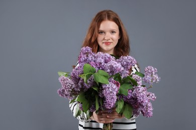 Photo of Portrait of beautiful teenage girl with lilac flowers on grey background