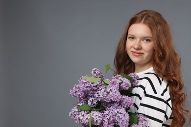 Photo of Beautiful teenage girl with bouquet of lilac flowers on grey background. Space for text