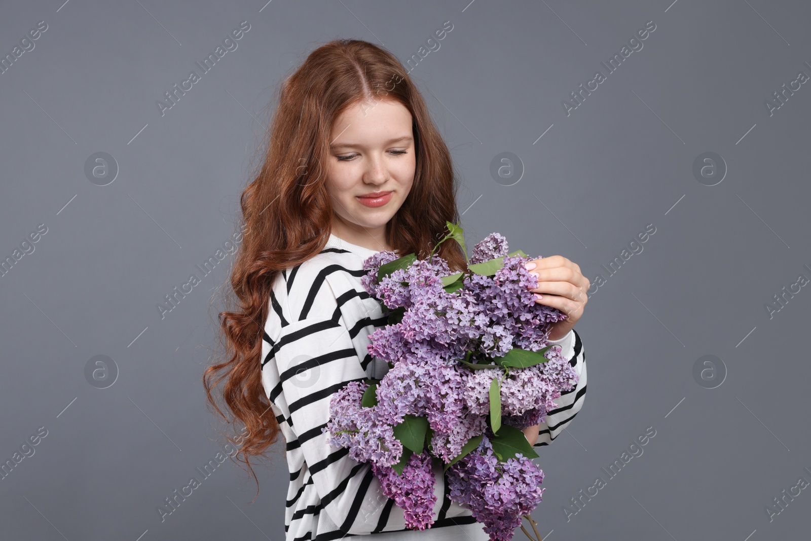 Portrait of beautiful teenage girl with lilac flowers on grey background Photo of Portrait of beautiful teenage girl with lilac flowers on grey background