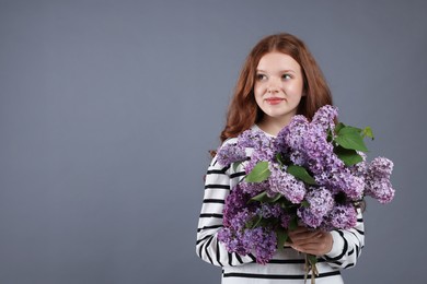 Photo of Beautiful teenage girl with bouquet of lilac flowers on grey background. Space for text