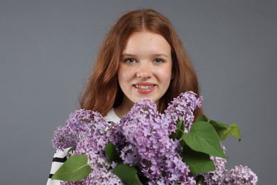 Photo of Portrait of smiling teenage girl with lilac flowers on grey background