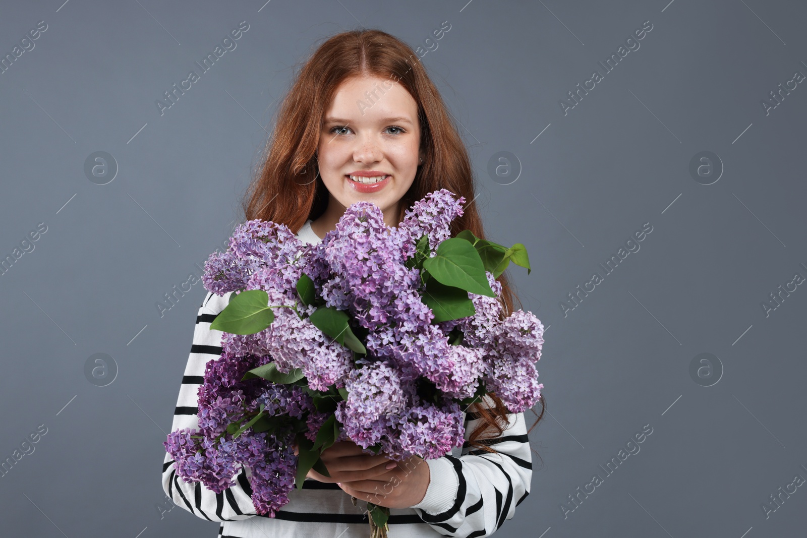Portrait of smiling teenage girl with lilac flowers on grey background Photo of Portrait of smiling teenage girl with lilac flowers on grey background
