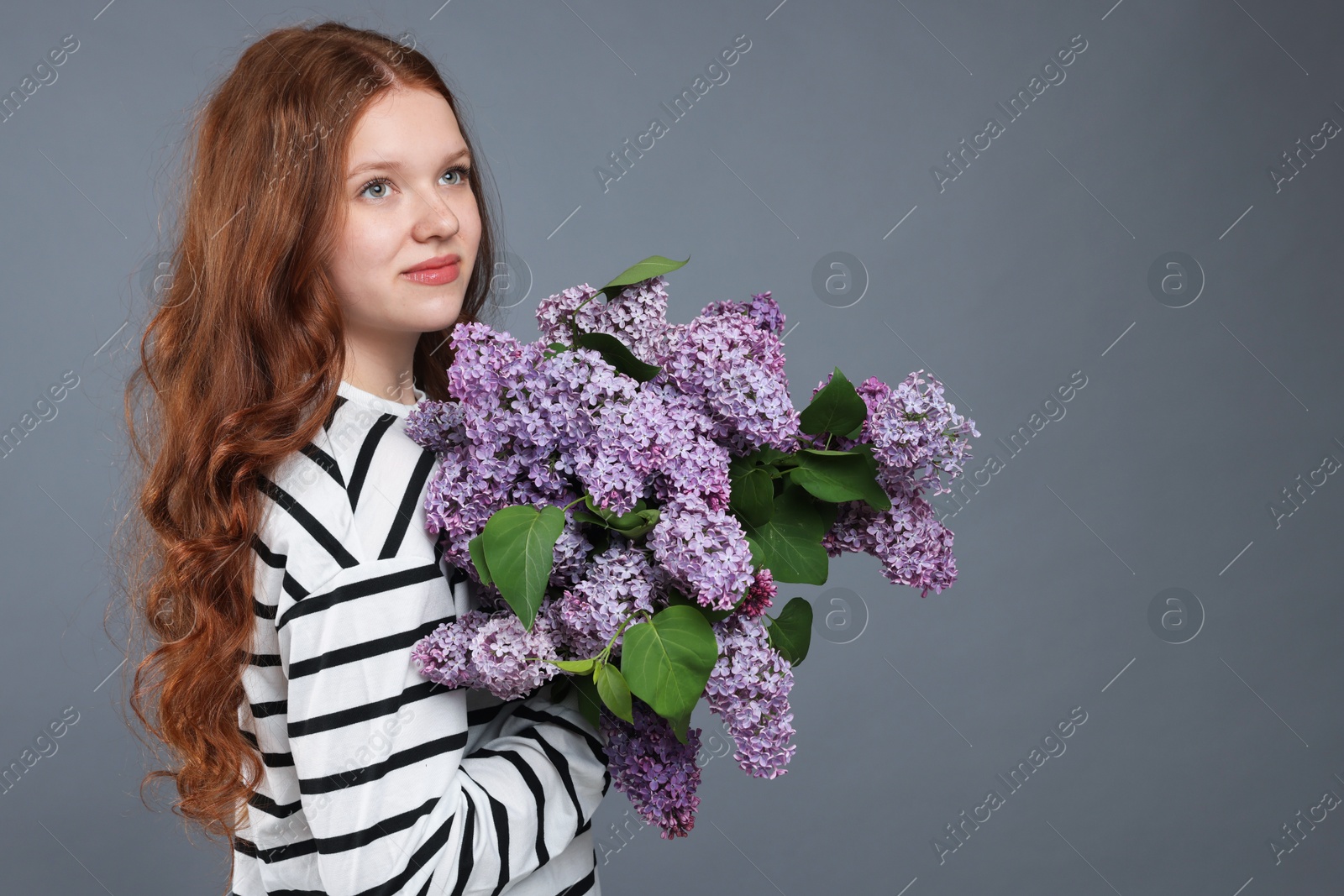 Beautiful teenage girl with bouquet of lilac flowers on grey background. Space for text Photo of Beautiful teenage girl with bouquet of lilac flowers on grey background. Space for text