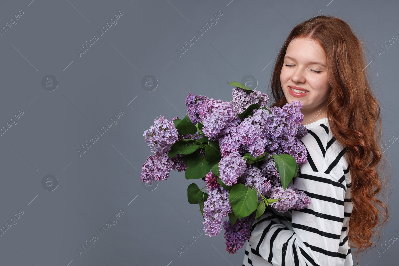 Smiling teenage girl with bouquet of lilac flowers on grey background. Space for text Photo of Smiling teenage girl with bouquet of lilac flowers on grey background. Space for text
