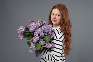 Photo of Portrait of beautiful teenage girl with lilac flowers on grey background