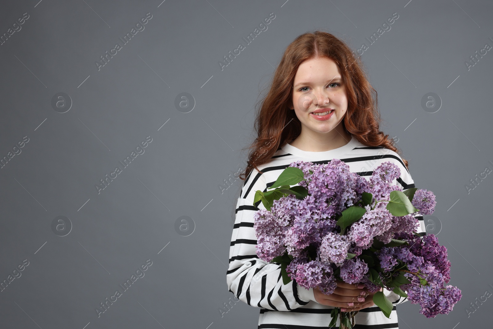 Smiling teenage girl with bouquet of lilac flowers on grey background. Space for text Photo of Smiling teenage girl with bouquet of lilac flowers on grey background. Space for text