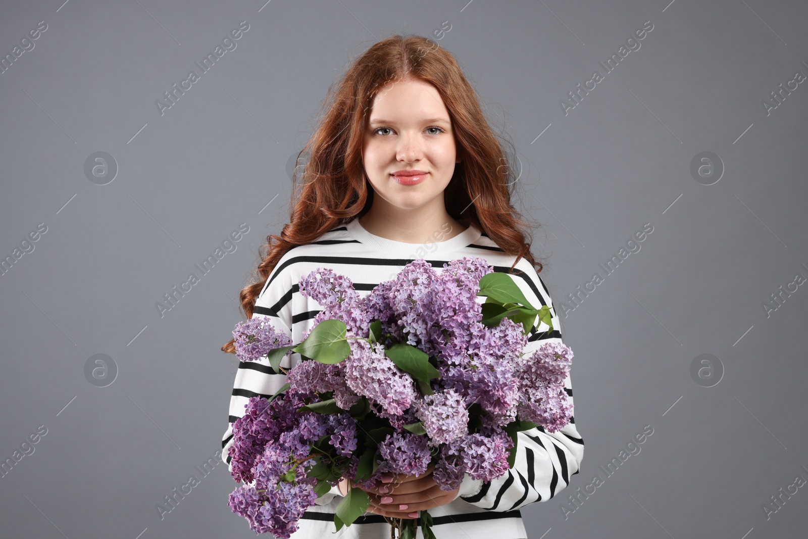 Portrait of beautiful teenage girl with lilac flowers on grey background Photo of Portrait of beautiful teenage girl with lilac flowers on grey background