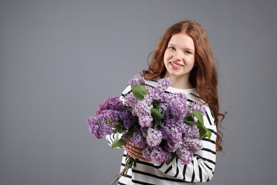 Photo of Smiling teenage girl with bouquet of lilac flowers on grey background. Space for text
