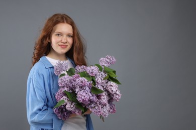Photo of Beautiful teenage girl with bouquet of lilac flowers on grey background. Space for text